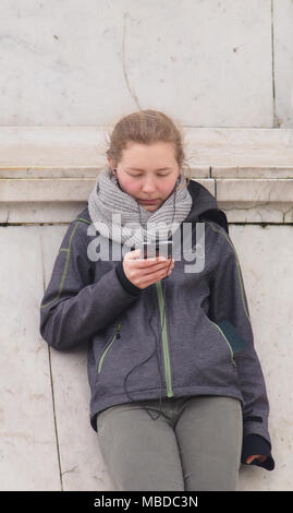 Une jeune femme appuyé contre la statue de la reine Victoria soutenir devant le palais de Buckingham, Londres en regardant son smartphone Banque D'Images