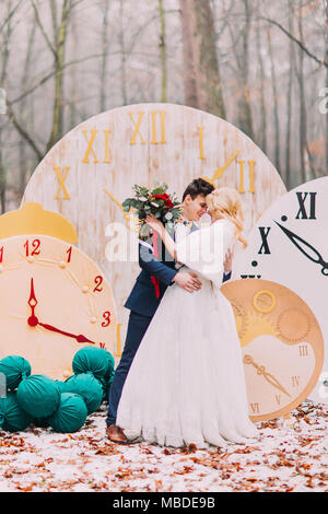 Happy wedding couple hugs doucement au grand vintage horloges en forêt d'automne. Décorations créatives Banque D'Images