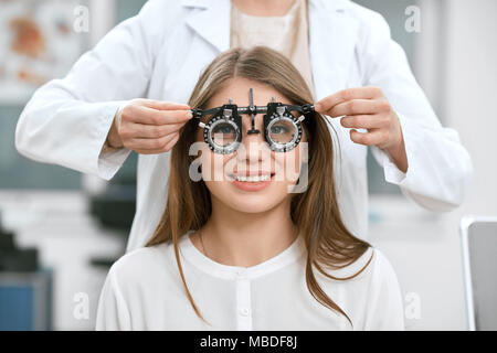 Young smiling girl est assis et à la caméra à vision au cours de la vérification. Ophtalmologiste est, à l'aide de l'équipement médical pour sauver et d'améliorer la santé de l'œil. Banque D'Images
