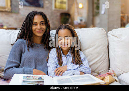 Portrait souriant, confiant les sœurs avec album photo sur canapé Banque D'Images