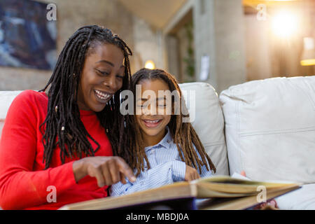 Smiling mother and daughter looking at album photo sur canapé Banque D'Images