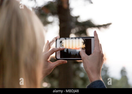 Femme avec téléphone appareil photo photographier le coucher du soleil Banque D'Images