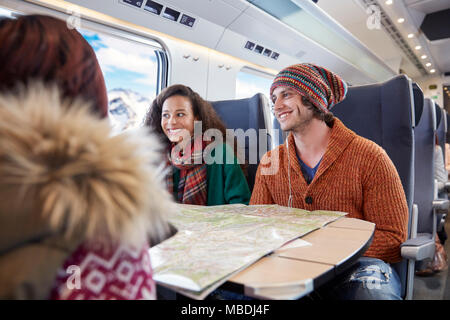 Smiling young friends planification avec des trains de voyageurs sur la carte Banque D'Images