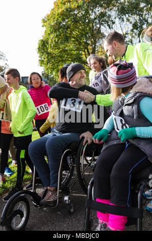 Man in wheelchair shaking hands with runner dans la foule lors de la course de bienfaisance Banque D'Images