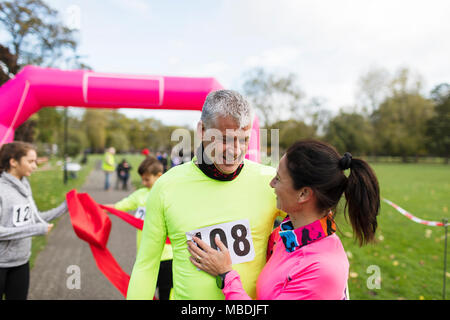 Couple heureux porteur hugging at ligne d'arrivée de charity run dans park Banque D'Images