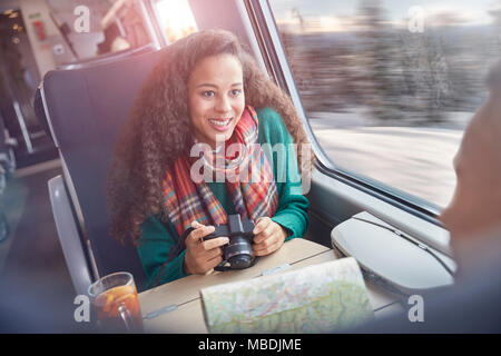 Souriante jeune femme avec appareil photo et carte Train de voyageurs d'équitation Banque D'Images