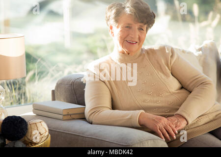 Smiling senior femme assise sur le canapé dans une maison de retraite Banque D'Images