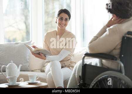 Les jeunes aidant la lecture d'un livre d'une femme senior dans un fauteuil roulant Banque D'Images