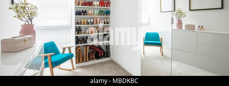 Fleurs sur fond blanc dans l'armoire vestiaire pastel intérieur avec fauteuil bleu à côté d'étagères avec des chaussures Banque D'Images