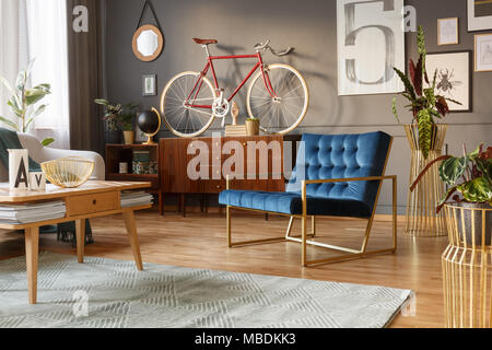 Fauteuil d'or et bleu, table en bois et rétro avec un vélo sur l'armoire en haut d''un salon intérieur Banque D'Images