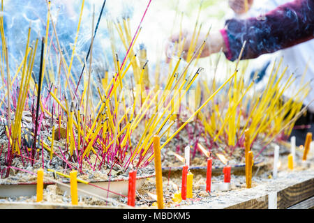 Vue rapprochée de la combustion d'encens plantés entre les pièces dans du sable sur une table lors d'une cérémonie bouddhiste, avec des chandelles à l'avant-plan. Banque D'Images