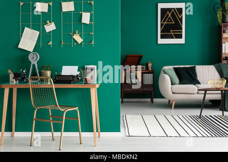 Or, chaise en métal par un bureau en bois avec réveil et machine à écrire dans un espace libre intérieur avec tapis et canapé lumineux Banque D'Images