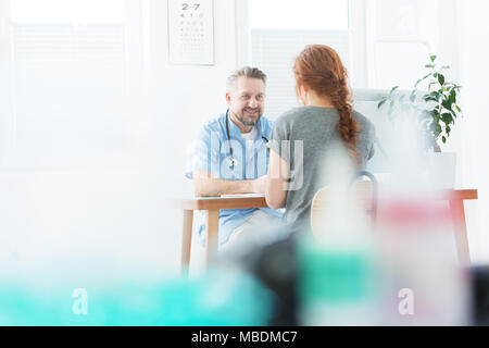 Beau médecin portant un uniforme de parler à une femme dans le bureau Banque D'Images