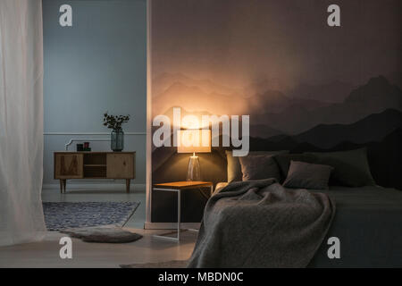 L'intérieur de chambre à coucher dans la nuit avec une lumière chaude de lampe sur une table de chevet près d'une armoire en bois Banque D'Images