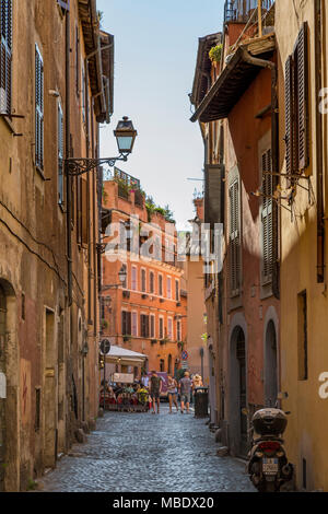 L'emblématique scène italienne avec des touristes marchant le long d'une voie pavée, au Trastevere de Rome, Italie, passé un restaurant avec des gens assis à l'extérieur Banque D'Images