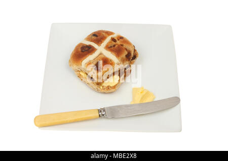 Hot cross bun sur une plaque avec du beurre et un couteau isolés contre white Banque D'Images