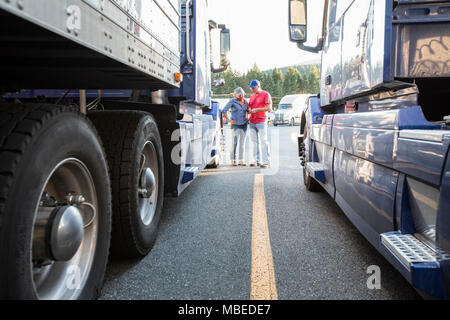 L'homme et de la femme de race blanche de l'équipe de conduite de camion allant plus de données sur un téléphone cellulaire en comité permanent entre les camions à un arrêt de camion. Banque D'Images
