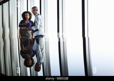 Black businesswoman et Asian businessman looking at un ordinateur portable et se reflètent sur le verre haut de bureau en face d'une banque de la fenêtre Banque D'Images