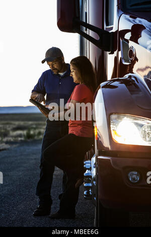 Mari et femme de l'équipe de conduite contrôle de leur ordinateur portable Connectez-vous tout en vous tenant à côté de la cabine de leur camion commercial après le coucher du soleil. Banque D'Images