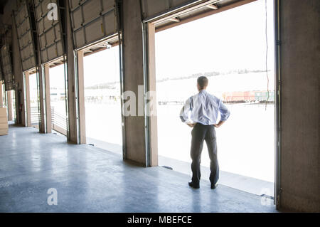 Homme Caucaaian en chemise et cravate debout dans la porte de chargement du nouveau entrepôt vide d'anticiper l'arrivée du premier chargement de camion de nouvelles affaires. Banque D'Images