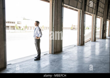 Homme Caucaaian en chemise et cravate debout dans la porte de chargement du nouveau entrepôt vide d'anticiper l'arrivée du premier chargement de camion de nouvelles affaires. Banque D'Images