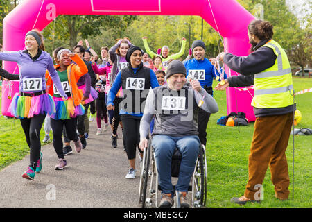 L'homme en fauteuil roulant et porteur de recevoir des médailles, traversant la ligne d'arrivée course de bienfaisance Banque D'Images