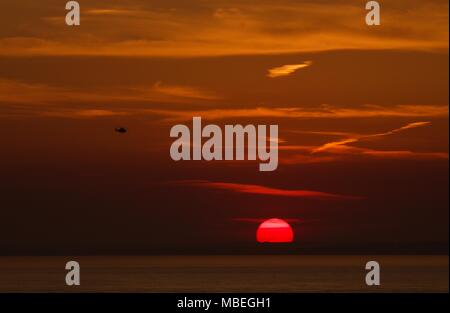 Red sky et sun sur le Solent avec le retour aux bases d'hélicoptère de garde-côtes après un appel de sauvetage Banque D'Images