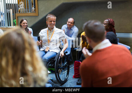 Public, l'écoute de l'orateur femelle avec microphone en fauteuil roulant Banque D'Images