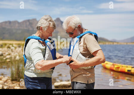 Couple actif mise sur les gilets de sauvetage, la préparation pour le kayak à sunny summer lakeside Banque D'Images