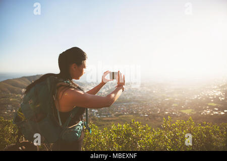 Backpacker femelle avec téléphone appareil photo photographier sunny vue sur la ville Banque D'Images