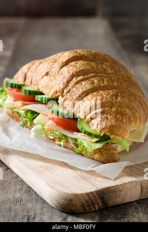 Croissant sandwich avec du fromage, du jambon et des légumes sur la table en bois Banque D'Images