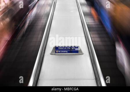 Une affiche qui dit 'Se débrouiller le droit' entre deux escaliers mécaniques en mouvement avec les gens, le métro de Londres, au Royaume-Uni. Banque D'Images