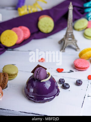 Gâteau rond lilas avec des macarons sur une planche de bois blanc, derrière un papier multicolores et d'une tour serpentine Banque D'Images