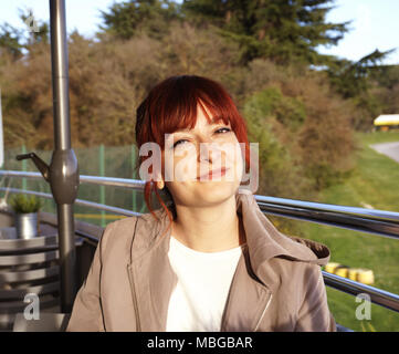 Belle jeune femme rousse assise sur la terrasse du café sur la journée de printemps ensoleillée et looking at camera and smiling Banque D'Images