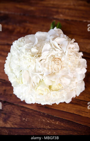 Shot vertical d'un bouquet de mariée avec les alliances sur elle, sur une table en bois foncé Banque D'Images