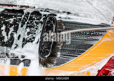 Détail de fenêtre arrière voiture jaune foncé lavé dans l'carwash. Coups de pinceau laissant en blanc mousse de savon et de shampooing. Banque D'Images