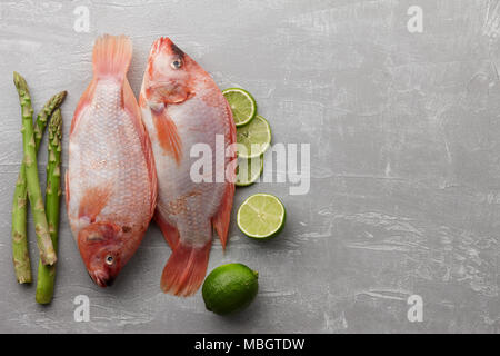 Deux matières de cuisson du poisson tilapia rouge avec la chaux et les asperges vertes sur fond noir en gris, vue du dessus Banque D'Images