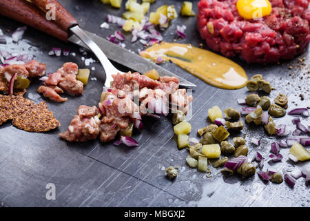 Steak tartare préparation. Le boeuf haché cru plat avec l'oignon, la moutarde, les câpres et les cornichons servi avec craquelins et d'oeuf de caille Banque D'Images