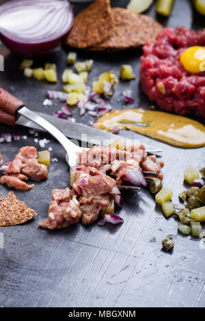 Steak tartare préparation. Le boeuf haché cru plat avec l'oignon, la moutarde, les câpres et les cornichons servi avec craquelins et d'oeuf de caille Banque D'Images