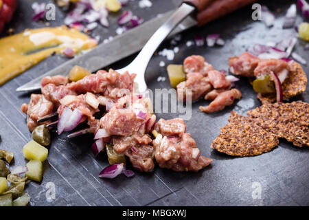 Steak tartare préparation. Le boeuf haché cru plat avec l'oignon, la moutarde, les câpres et les cornichons servi avec craquelins et d'oeuf de caille Banque D'Images