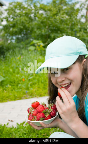 Petite fille mange fraise dans jardin Banque D'Images