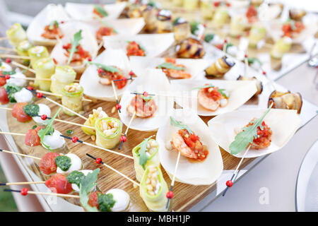 Crevettes délicieux et des tranches de tomate sur un bateau en bois. Rouleaux de courgettes avec les pignons de pin. Table de buffet savoureux. Fête de l'été à l'extérieur. Concept de restauration Banque D'Images