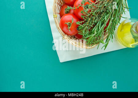 Des tomates rouges mûres Le romarin le thym dans l'huile d'Olive panier en osier blanc Serviette en bouteille sur fond vert. L'imitation de la couleur du drapeau National Italien Banque D'Images