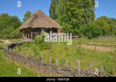 Une vieille maison de bois entre les arbres et l'herbe, entourée de barrière en bois Banque D'Images