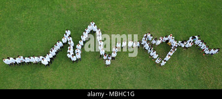 Kiev, Ukraine - 22 Avril 2018 : les étudiants en médecine debout sur l'herbe, faire vivre coeur graphique. Les personnes de nationalités différentes. Physycians vêtus de blanc uniforme médical. L'action de bienfaisance. Banque D'Images