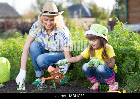 Cute kid girl aide sa mère à s'occuper de plantes. Mère et sa fille engagée dans le jardinage dans la cour. Concept de printemps, de la nature et des soins. Banque D'Images