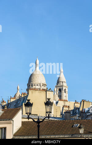 Le dôme et le clocher carré de la Basilique du Sacré Coeur à Paris qui sort au-dessus des toits des bâtiments avec un lampadaire en premier plan. Banque D'Images