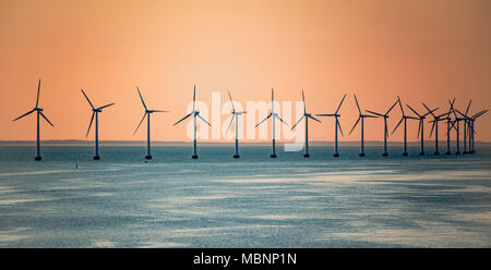 Parc d'éoliennes au large des côtes de l'océan au coucher du soleil sur les rangs Banque D'Images