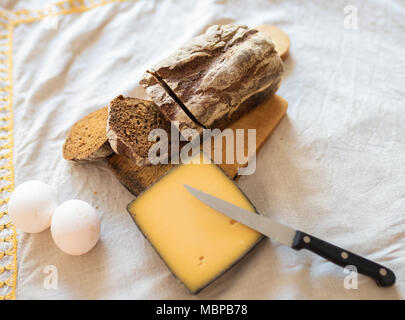 Une tranche de fromage, deux œufs et un morceau de pain sur une table avec une nappe en lin. Vue d'en haut. Banque D'Images