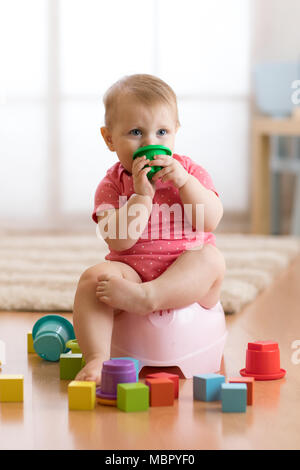 Bébé est assis sur un pot pour enfants, toilettes, jouer avec des jouets Banque D'Images